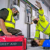 Two workers in hard hats performing CPR on an injured person