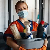 Cleaner in a face mask showing her cleaning products