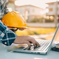 Person holding a hard hat using a laptop