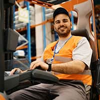 Happy forklift operator working at distribution warehouse