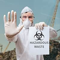 In a hazmat suit, a man displays a sign with a hazardous waste symbol, highlighting the importance of environmental safety.