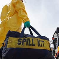 Rescue personnel wearing yellow chemical protective clothing holding a spill kit