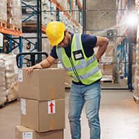 Man in factory showing signs of back pain while moving boxes