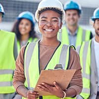 Young woman with a hardhat and safety glasses holding a clipboard