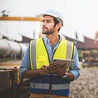 A man in a hard hat and vest holding a tablet