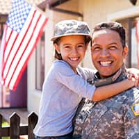 Soldier in fatigues holding a child with American flag in the background