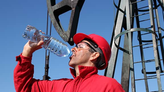 A man wearing a hard hat takes a refreshing drink of water, emphasizing safety and hydration on the job site.