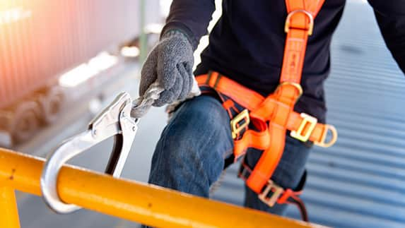 Individual in an orange safety harness grips a hook, demonstrating safety measures in a professional setting.