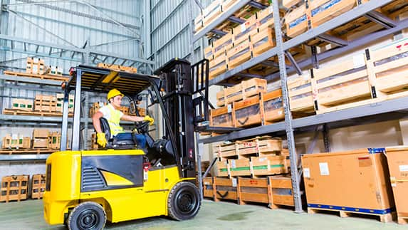 A worker operates a forklift inside a warehouse.