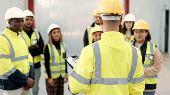 A group of individuals wearing yellow vests and hard hats, engaged in a construction or safety-related activity.