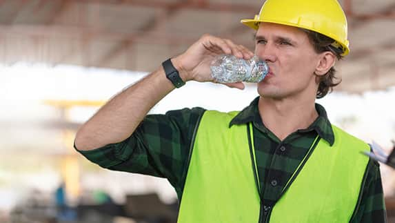 A man wearing a hard hat takes a refreshing drink of water, emphasizing safety and hydration on the job site.